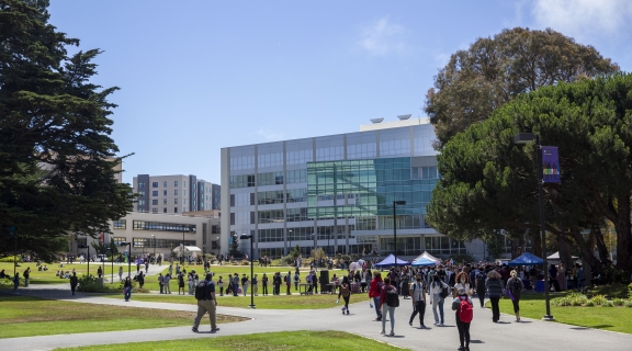 Students walking across the campus quad space with event tents and the library in the background